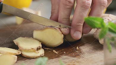 Male hand cuts ginger with a knife on a board