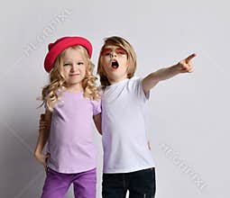 Little positive blond baby girl and boy in stylish casual clothing and accessories standing, hugging each other feeling cheerful