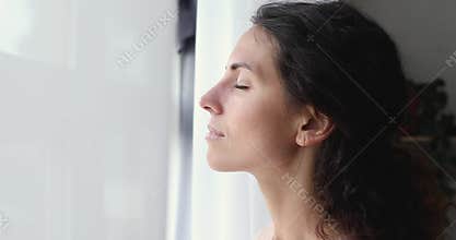 Calm lady taking deep breath of fresh air at window