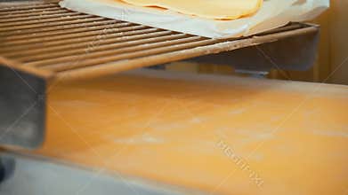 Rolling puff pastry on a machine for making pies and rolls.