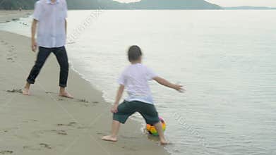 Happy family with father and son doing activity playing football on the beach for leisure