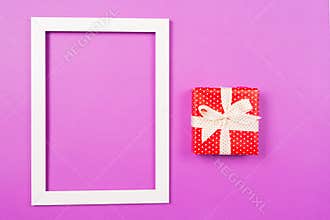 Red Gift box and white picture frame on purple background. St Valentine`s Day Mothers`s Day Wedding Birthday concept