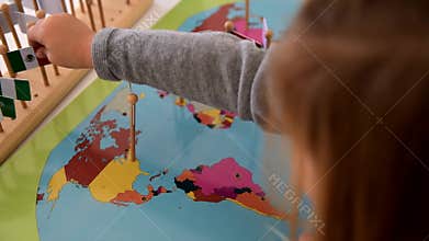 Little student girl trying match flags with countries on a Montessori map