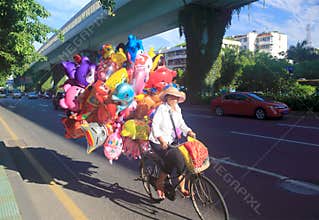 Woman riding a bicycle selling balloons, srgb image.