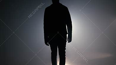 Silhouette of man is walking through smoky studio or scene right from camera