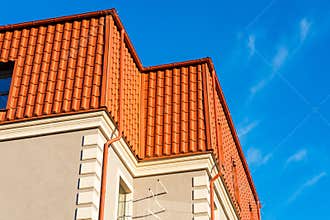 Newly installed construction frame house rain gutter system on the red metal roof top.