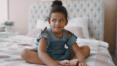Pretty happy smiling afro american girl child with curly hair sits on bed in cozy bedroom wear blue chintz dress