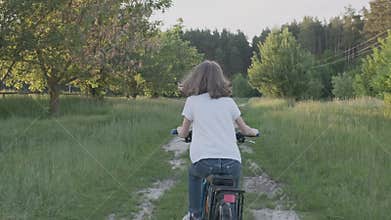 Kid girl rides a bike, girls first cycling success, sunset country road, natural landscape background, back view