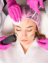 Close up of the beautiful face of a young woman. Many hands holding cosmetology tools near face of a patient