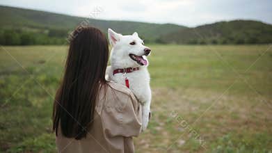 Young woman carries on hands and kissing a white swiss shepherd dog on the outdoor lawn.