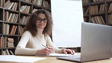 Smiling hispanic school math teacher looking at camera in classroom with laptop.