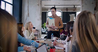 Young confident Asian coach businessman leading team brainstorming seminar at loft trendy multiethnic office slow motion