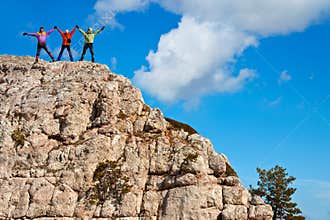 Hikers at the top of a rock with their hands up