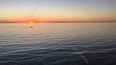 Silhouette of man paddling in kayak with dramatic sunset