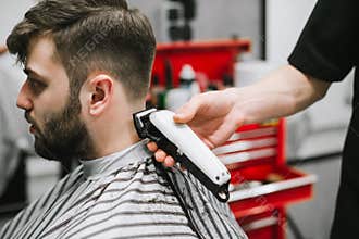 Closeup photo of a barber`s hand with a haircut, creates a stylish hairstyle for a bearded man in a hair salon for men.
