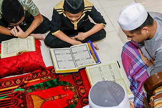 Malaysian muslim kids reading the book of the holy Quran to celebrate the holy Ramadan Kareem feasting