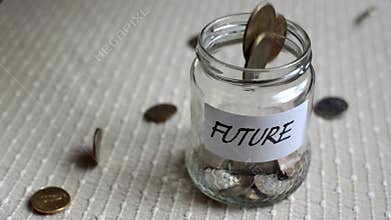 Coins filling and overflowing a clear medium sized glass jar