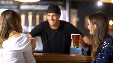 Cute barman smiling while serving beer to a couple of pretty girls waiting at the bar tab