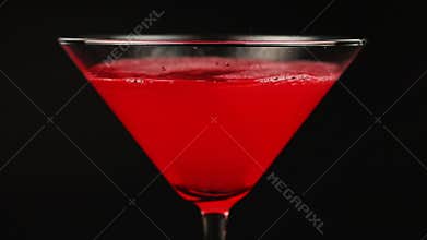 Pouring red cocktail in martini glass on black background