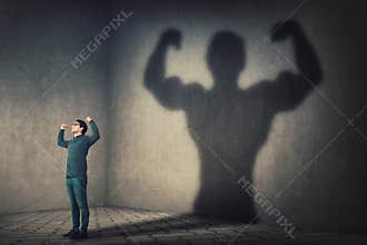 Confident man flexing muscles imagine super power as casting a shadow of muscular bodybuilder showing biceps. Strong person facing