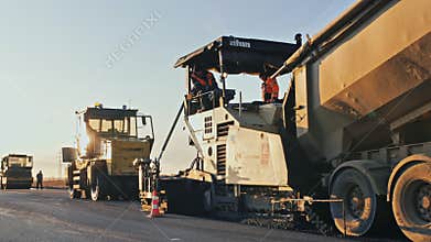 Novosibirsk region, September 4, 2020. Road construction at sunset. Loading the asphalt mixture into the paver. Road