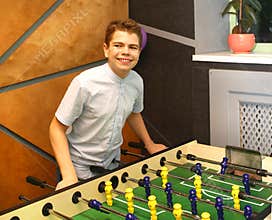 Boy teenager in a blue shirt plays in a table football with figures of football players of both teams in a wooden box in the