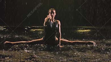 A graceful dance with acrobatic elements performed by a slender gymnast under streams of rain and splashing water. Close