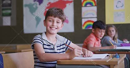 Boy smiling while sitting on his desk at school