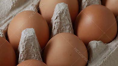 Brown organic chicken eggs in a cardboard box with a chicken feather