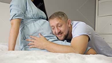 Happy man stroking and kissing the belly of his pregnant wife. Waiting for the birth of a child.