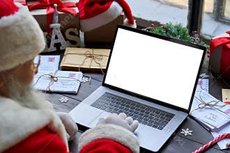Santa Claus using laptop computer mock up white screen sitting at table.