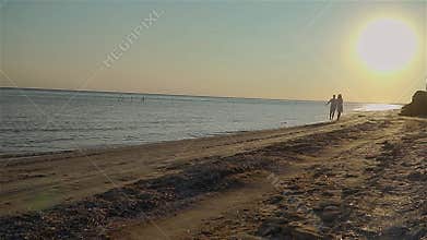 Young couple of man and woman running barefoot along sea sand beach at sunset