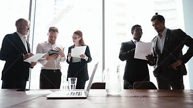 Portrait of multinational business team of businessmen and businesswoman reading documents of window