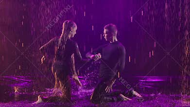 Happy woman and man dance emotionally swift jive in slow motion on rain pools. Wet couple of dancers under drops of rain
