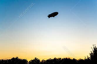 Zeppelin in evening sky, Airship in backlight in bright sky. Zeppelin in sky during sunset.