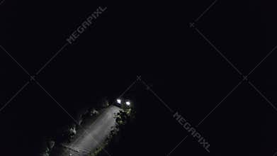 Car moving on countryside road in dark night drone top view. Car headlights illuminating night road in darkness