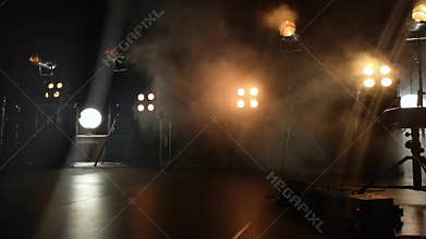 Close-up video of a concert stage and lighting fixtures on it. Smoke from a smoke installation gently breaks yellow light and crea