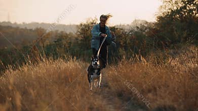 Woman running with dog on nature at sunset. Carefree enjoying a summer time with pet.