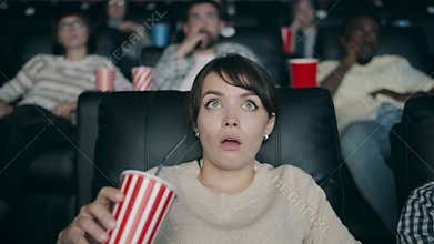 Slow motion of beautiful woman watching film in cinema with open mouth drinking