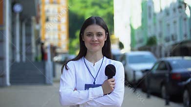 Female journalist with microphone and press pass looking at camera on street