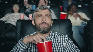 Slow motion of grey-haired man chewing popcorn watching scary movie in cinema