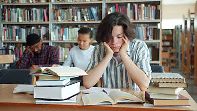 Exhausted teenager touching face then studying in university library at desk