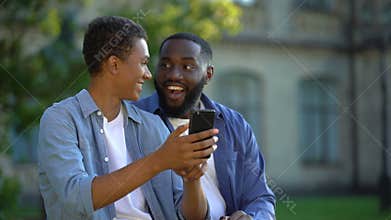 Happy male teenager showing smartphone application to father sitting outdoors