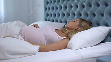 Pregnant woman feeling unwell lying in bed, sleep disorder, health problems