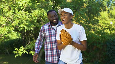 Happy father praising son playing baseball in park, family support, connection