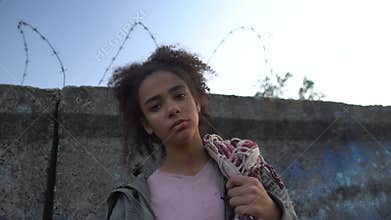 Biracial teenage girl holding bag, dreaming to escape from refugee camp, poverty