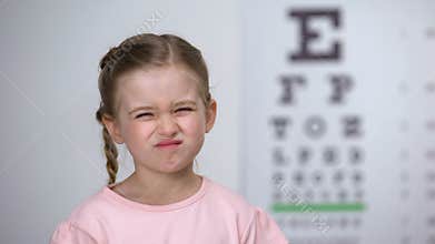 Little girl squinting eyes, suffering blurred vision, diagnostics of astigmatism