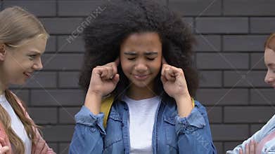 Biracial teenage girl covering ears from bullying, mockery of classmates, racism