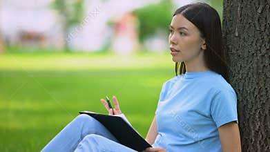Female student writing essay sitting park, journalist working article, notes