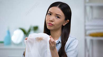 Upset asian housewife showing coffee stain on shirt at camera, laundry service